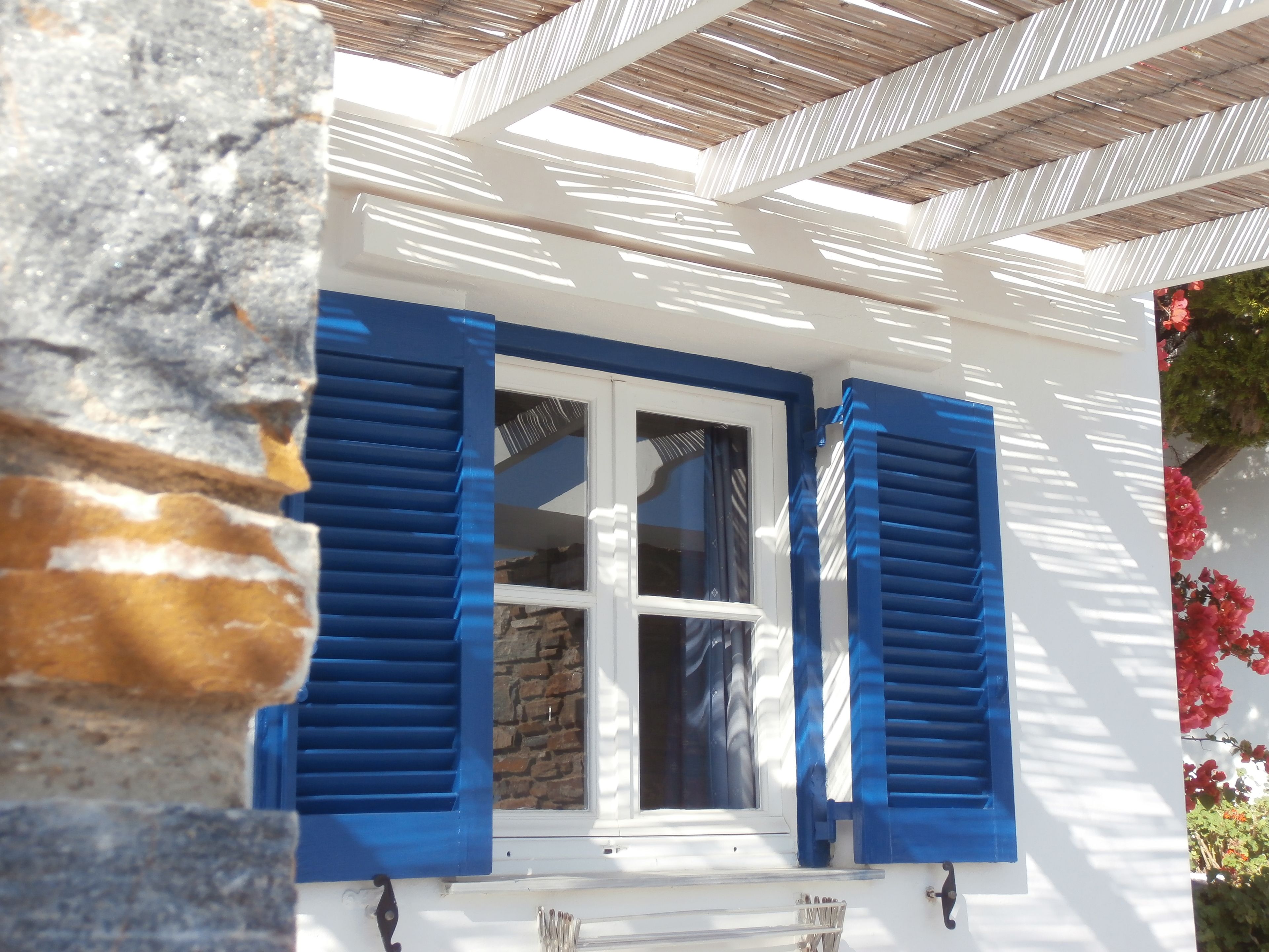 A window with blue shutters, a stone wall, and a wooden ceiling structure.
