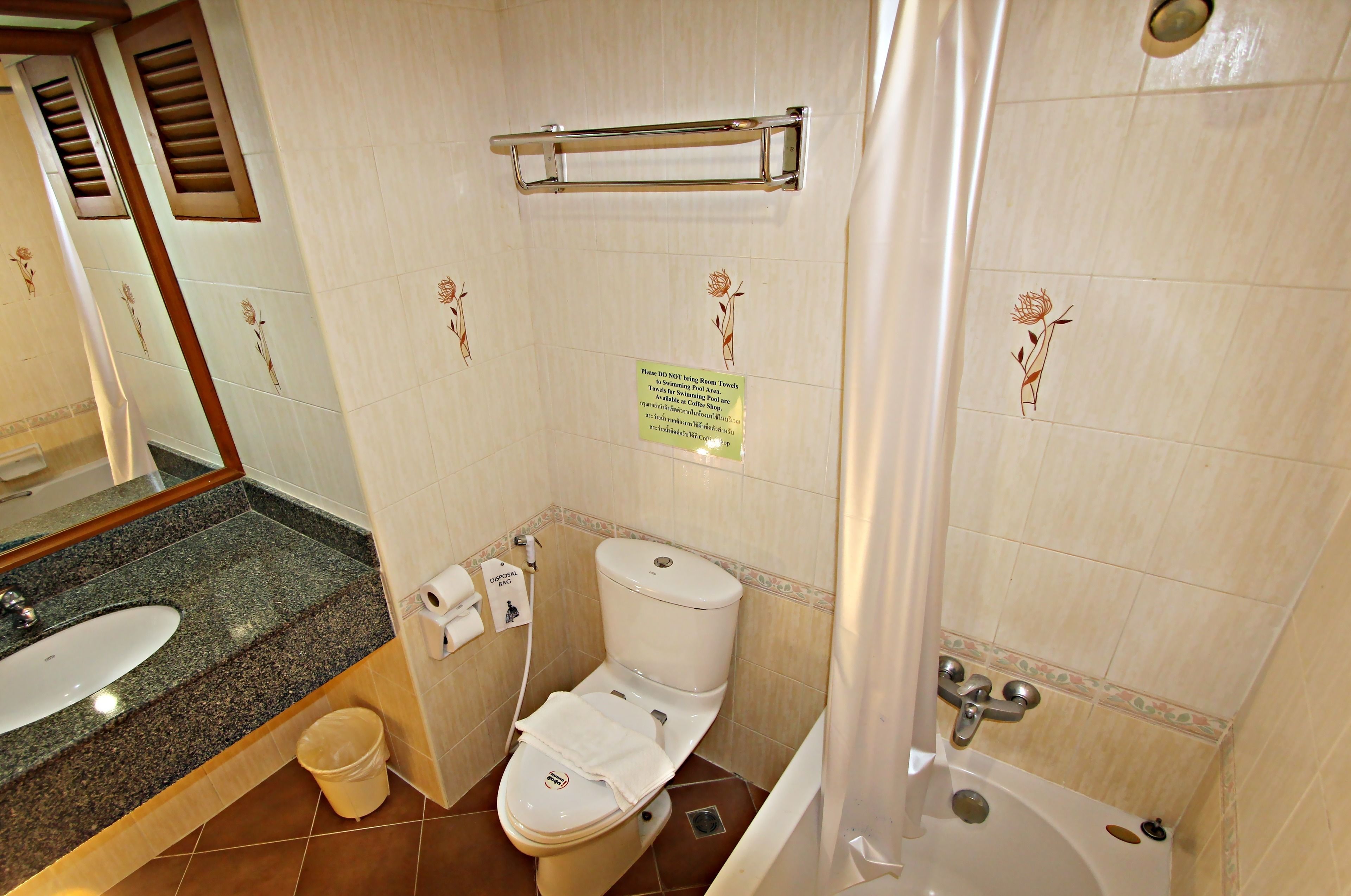 A bathroom with a toilet, sink, and bathtub. There is a towel rack above the toilet and a sign on the wall.