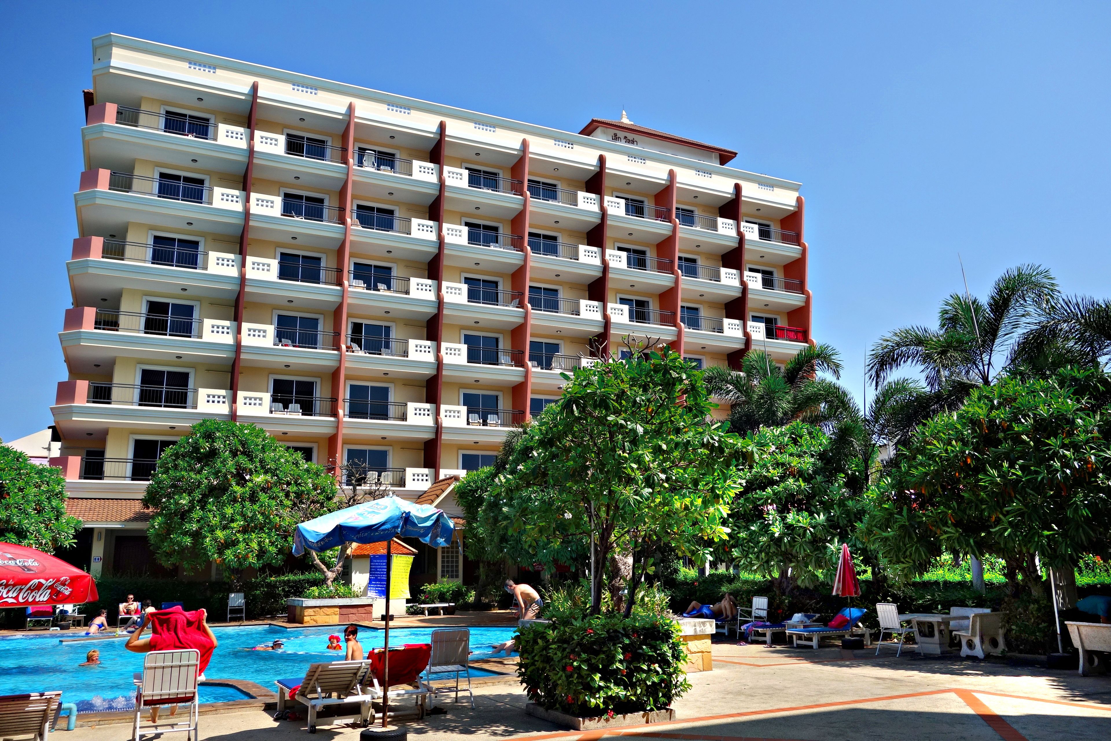 A hotel with a swimming pool, outdoor seating, and lush greenery.