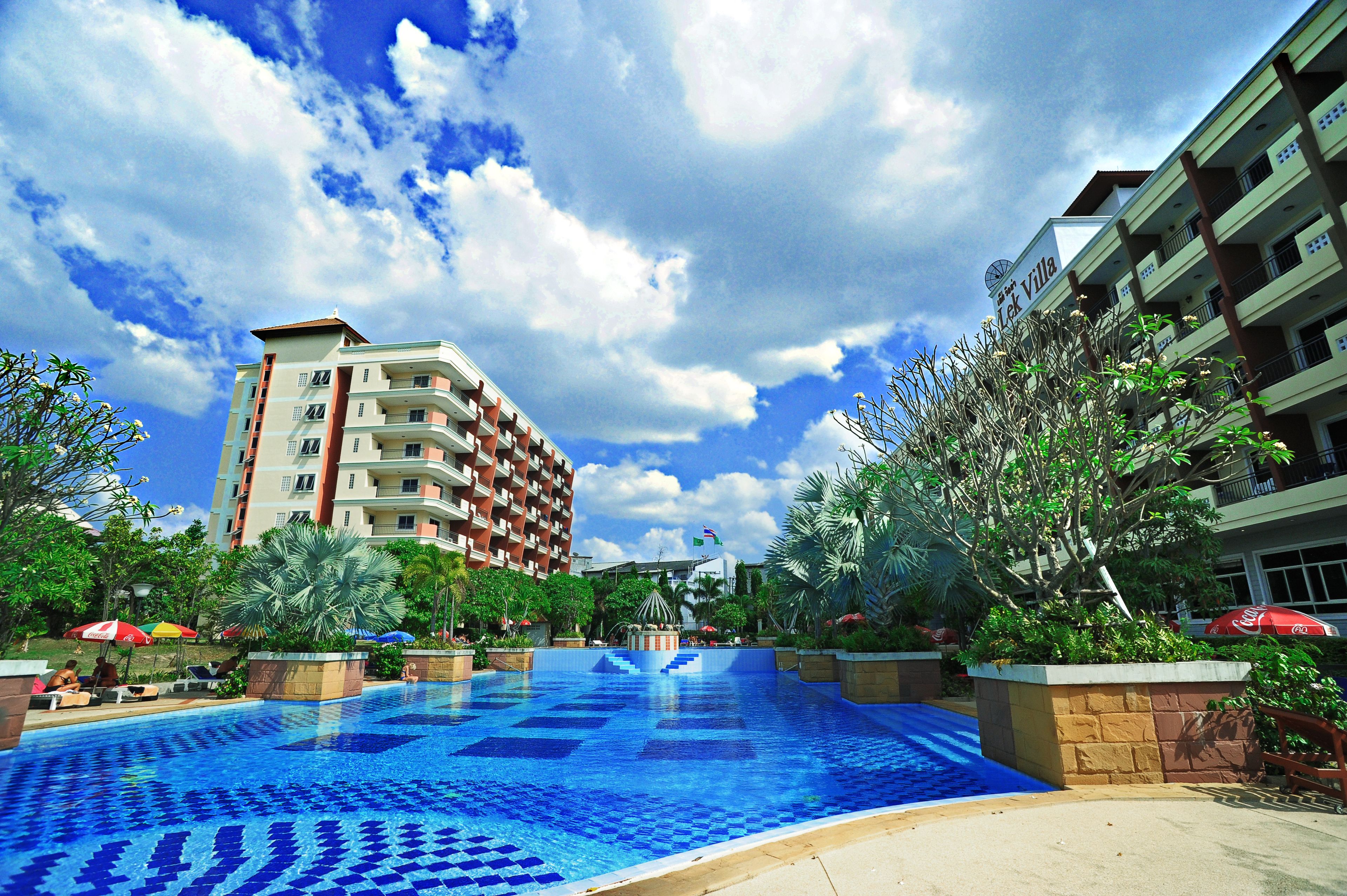 A hotel with a swimming pool, palm trees, and a clear sky.