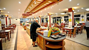 Un restaurant spacieux, doté de nombreuses tables et chaises, d’un buffet proposant une variété de plats et de ventilateurs de plafond.