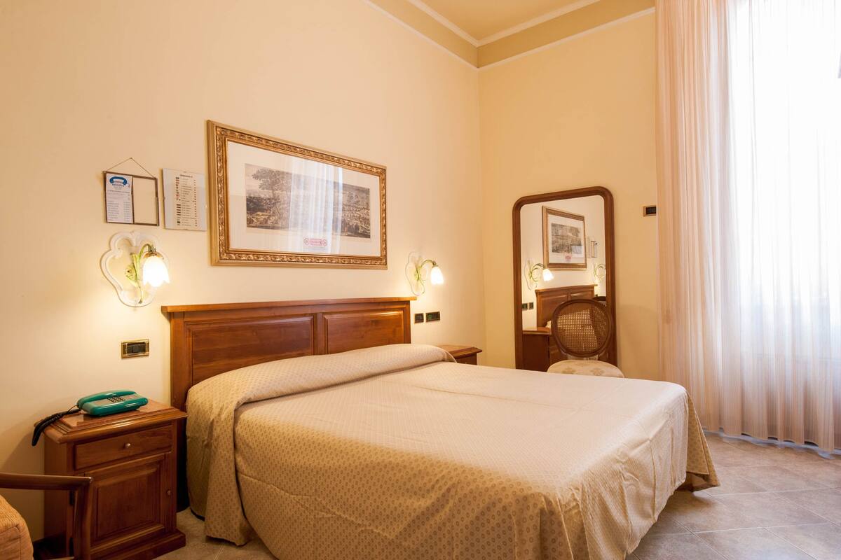 Una habitación de hotel con una cama grande, mesitas de noche, un espejo y cuadros en la pared.
