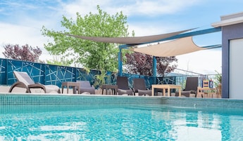 Una piscina con sillas de descanso y una zona sombreada.