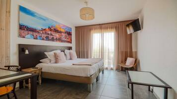 A hotel room with a bed, a desk, a chair, a TV, and a painting of a bridge.