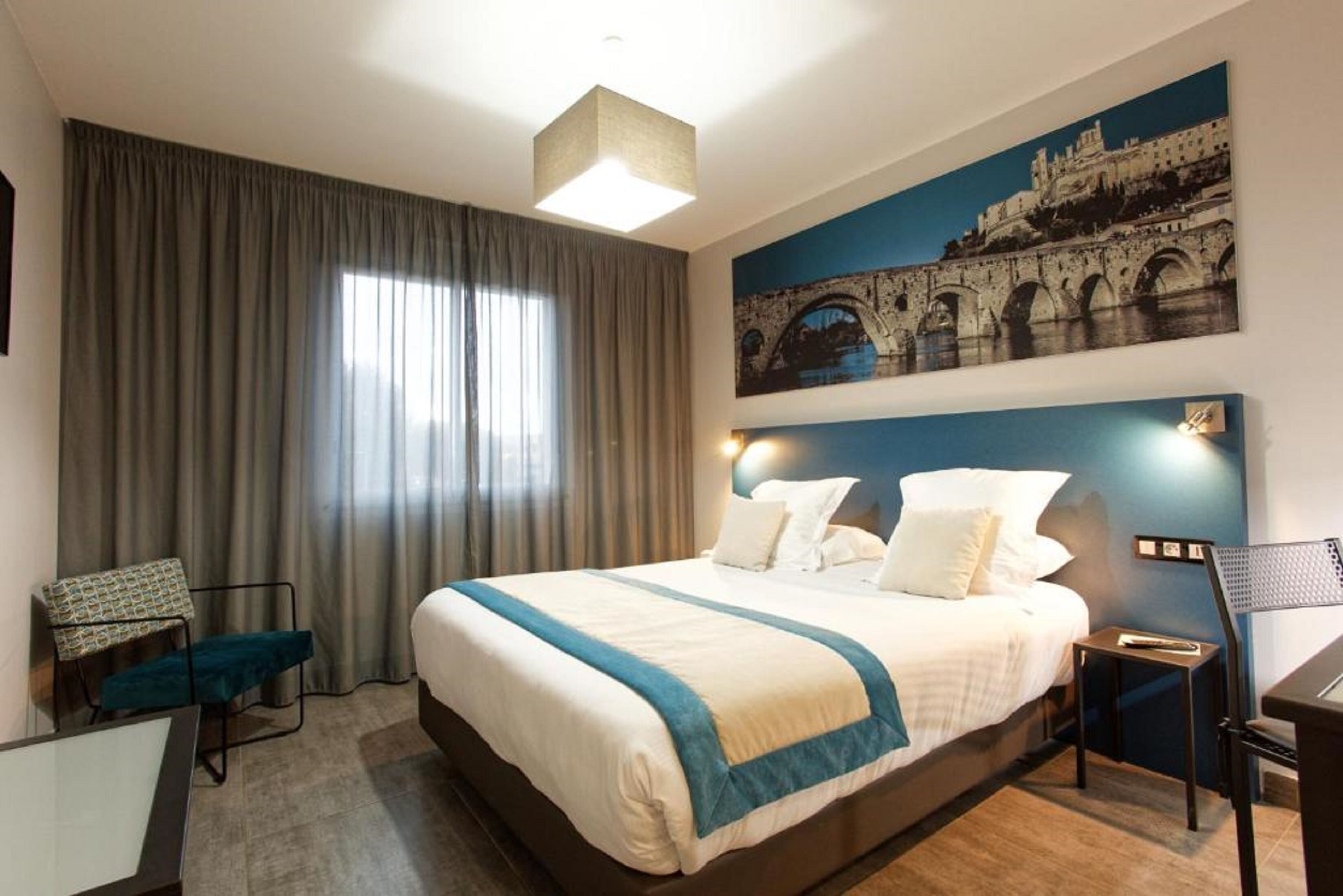 Une chambre d’hôtel avec un grand lit, un bureau, une chaise et un tableau représentant un pont accroché au mur.
