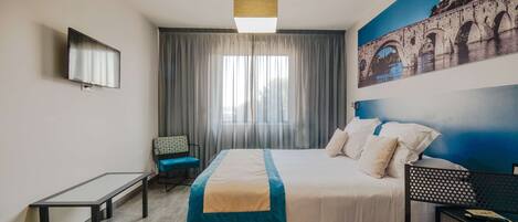 A hotel room with a bed, a desk, a chair, a TV, and a large window with curtains.