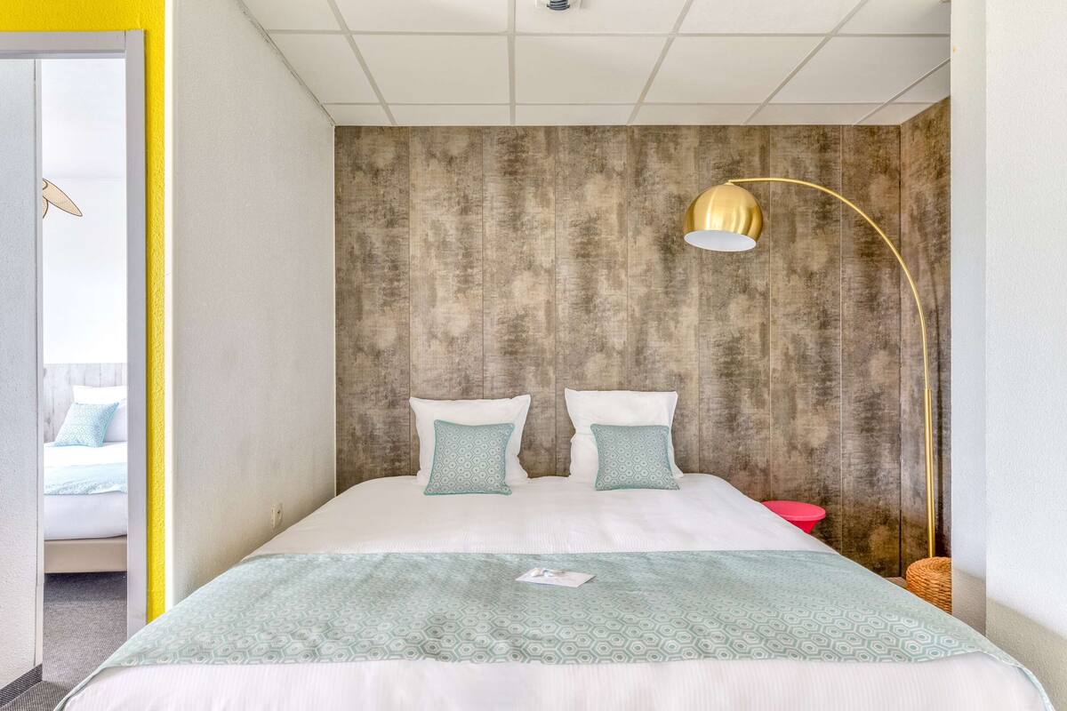 A bedroom with a bed, two pillows, a bedside table, a lamp, and a wall with a textured pattern.