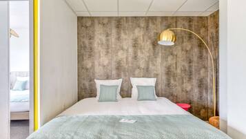 Un dormitorio con cama, dos almohadas, una mesita de noche, una lámpara y una pared con textura.