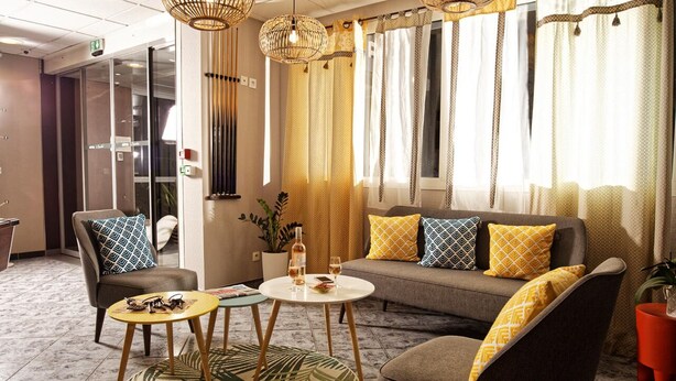 A modern hotel room with a sofa, two armchairs, a coffee table, and a dining table. There are decorative lamps, curtains, and a potted plant. - Sure Hotel by Best Western Beziers Le Monestie (Boujan-sur-Libron)