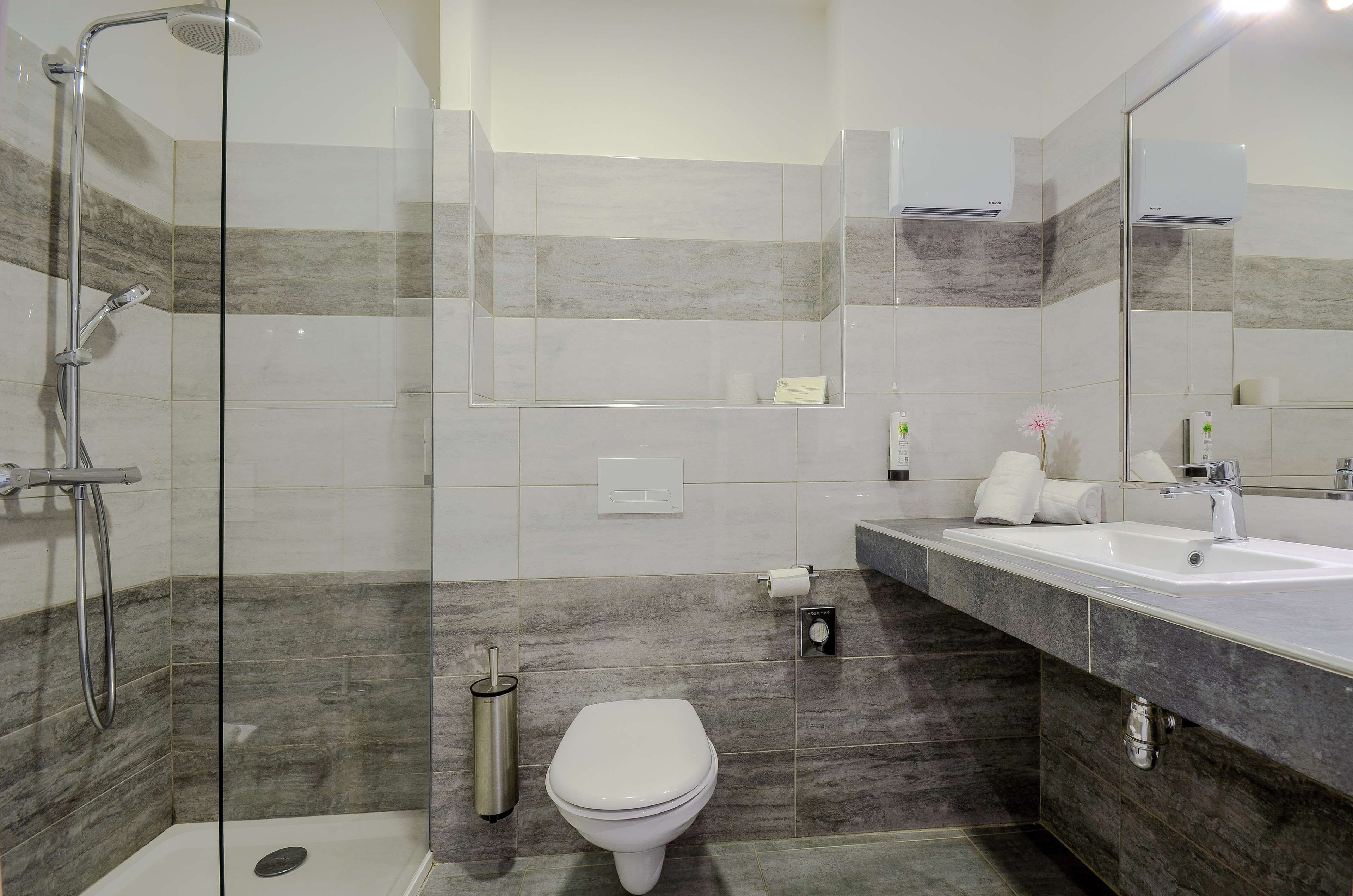 Un baño moderno con ducha envuelta en vidrio, inodoro y lavamanos con espejo.