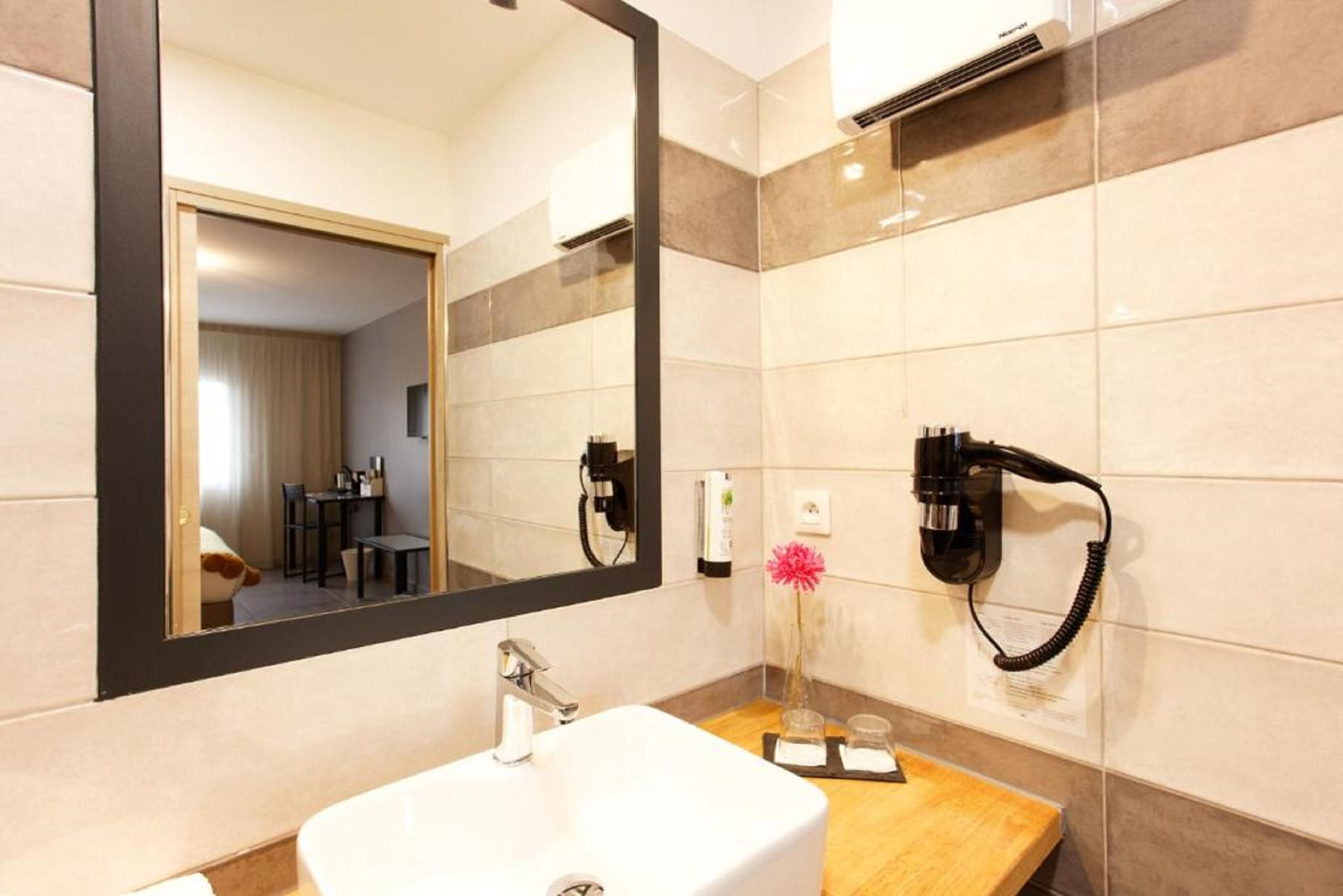Une salle de bain moderne avec un grand miroir, un lavabo blanc, un sèche-cheveux fixé au mur et un meuble-lavabo en bois.