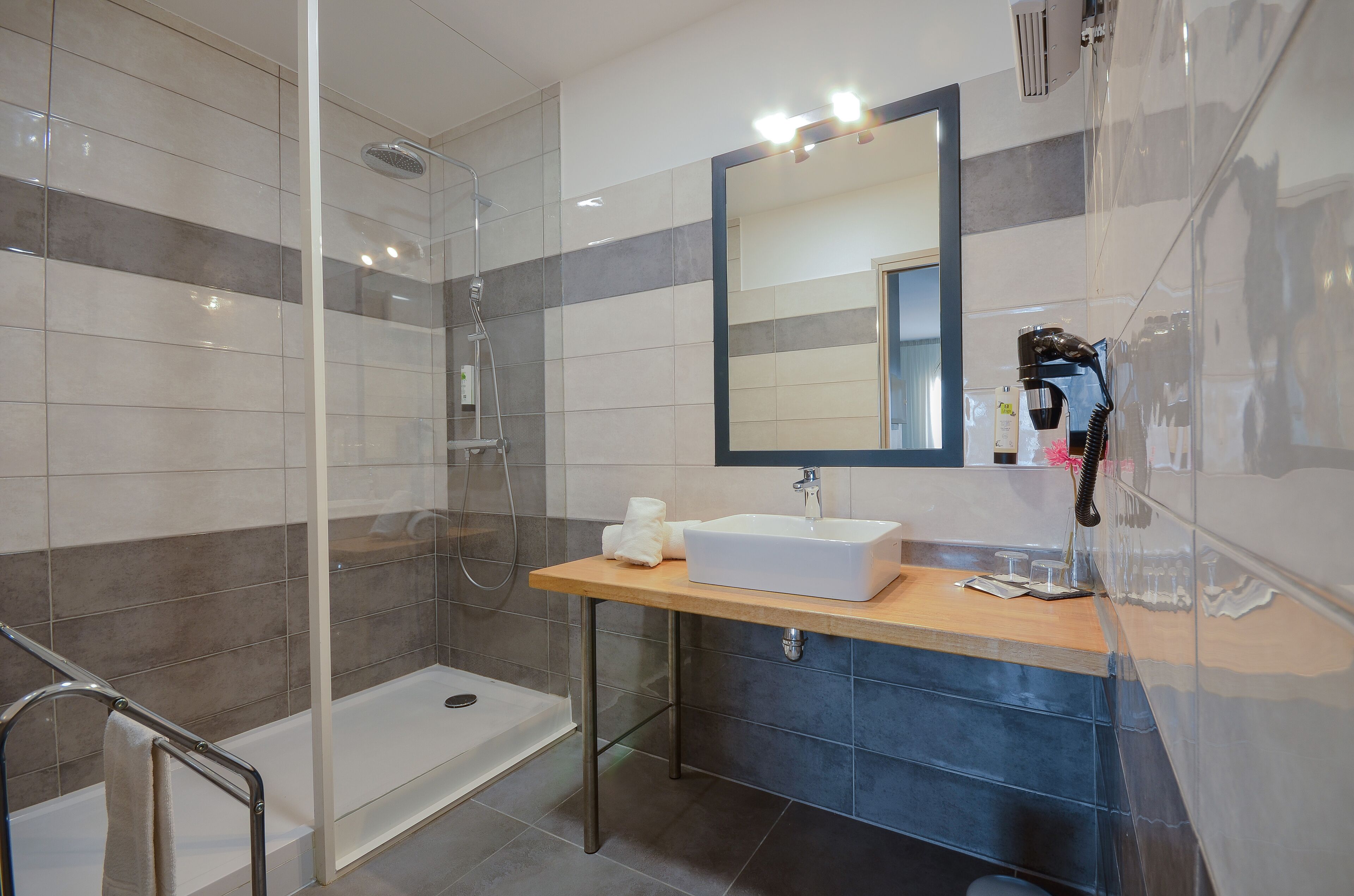 A modern bathroom with a glass-enclosed shower, a sink with a mirror, and a wooden vanity.