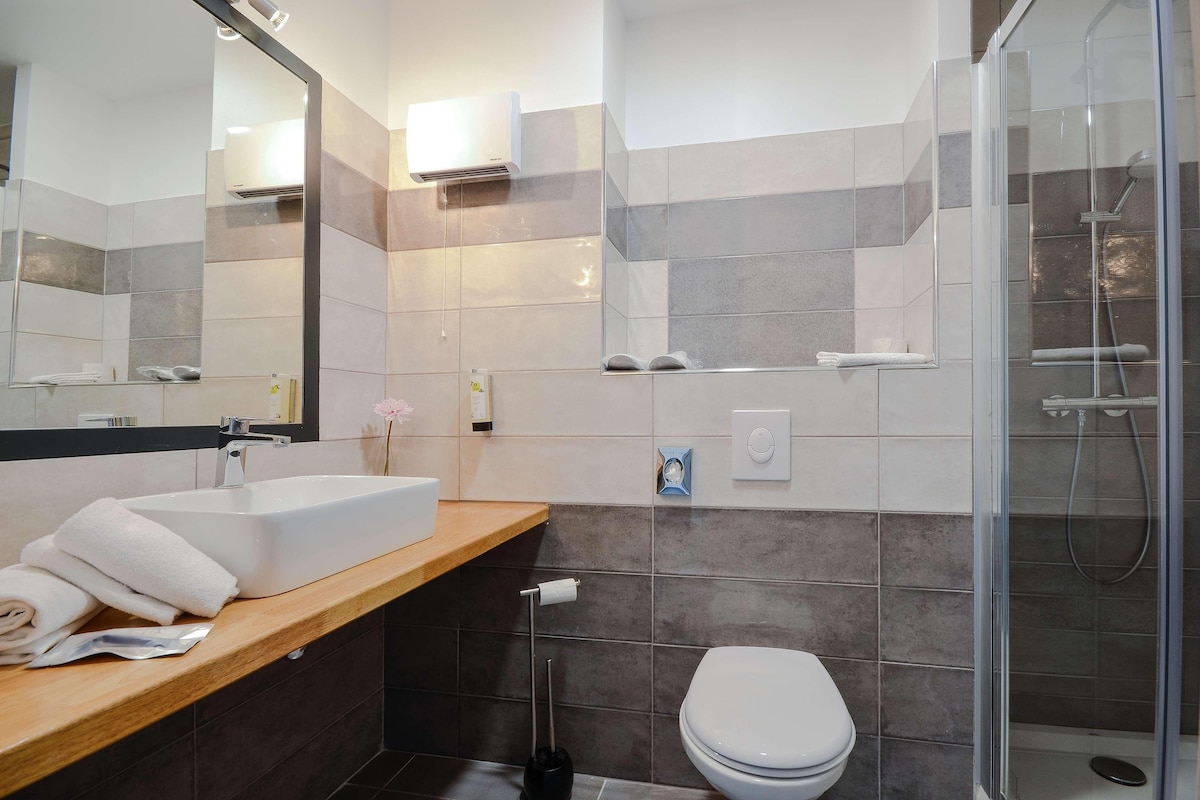 Une salle de bain moderne équipée d’un lavabo, d’un miroir, de toilettes et d’une douche à parois de verre.