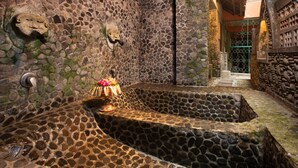 A stone-walled spa area with a central hot tub, a decorative mask on the wall, and a small altar with flowers. - Ketut's Place Bed & Breakfast Ubud (Ubud)