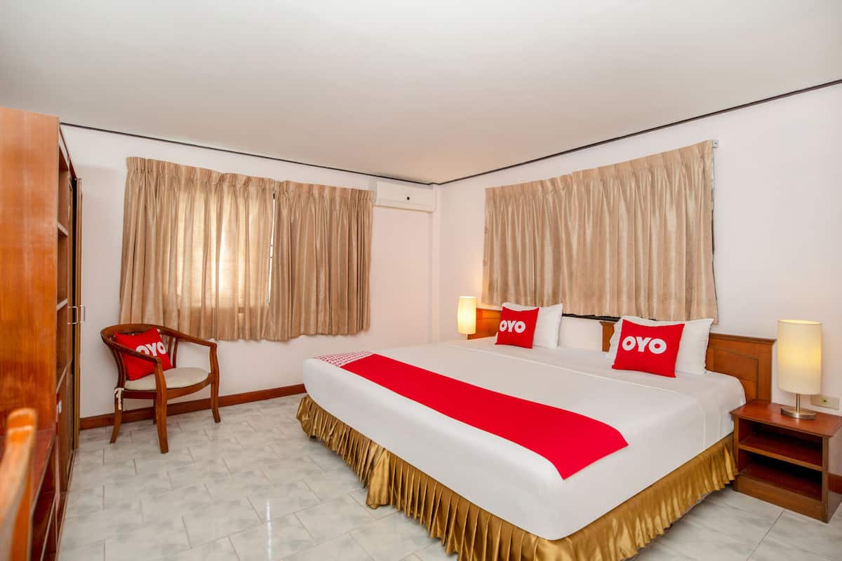 A hotel room with a large bed, two bedside tables, a wooden chair, and beige curtains.
