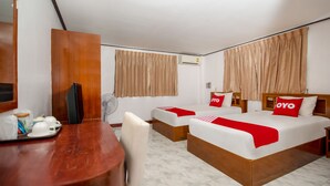 A hotel room with two beds, a wooden desk, a chair, a fan, and a small table with cups and a jar. - OYO 288 The Minotel Hotel (Patong)