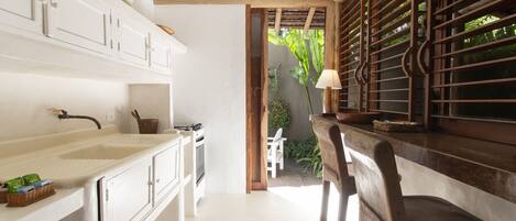 Una cocina con armarios blancos, encimera de madera y vistas al exterior con vegetación.