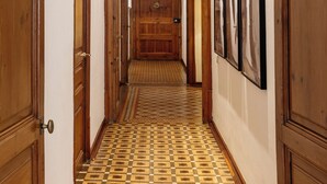 Un passadís amb portes de fusta, rajoles de terra amb un disseny i quadres amb marc a la paret.
