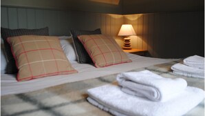 A neatly made bed with a checkered pillow, a bedside lamp, and folded towels on a marble-patterned bedspread. - The Queens (Carlisle)