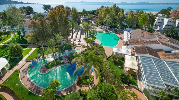 Un complexe hôtelier doté d’une grande piscine, de palmiers et offrant une vue sur la mer.