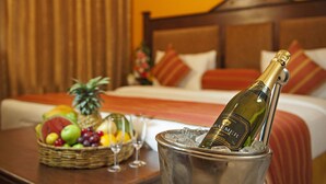 Una cama con cabecera de madera, una cesta de frutas variadas, una botella de champán en un balde y una copa de vino sobre una mesa.