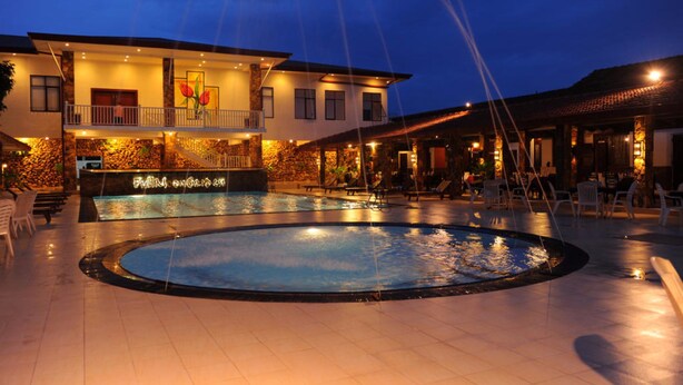 Un hotel con piscina, mobiliario exterior y una entrada bien iluminada.