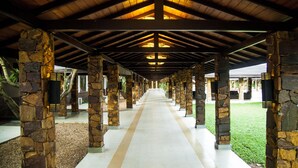 Un paseo techado con pilares de piedra y piso de baldosas, que conduce a un edificio con fachada de vidrio.