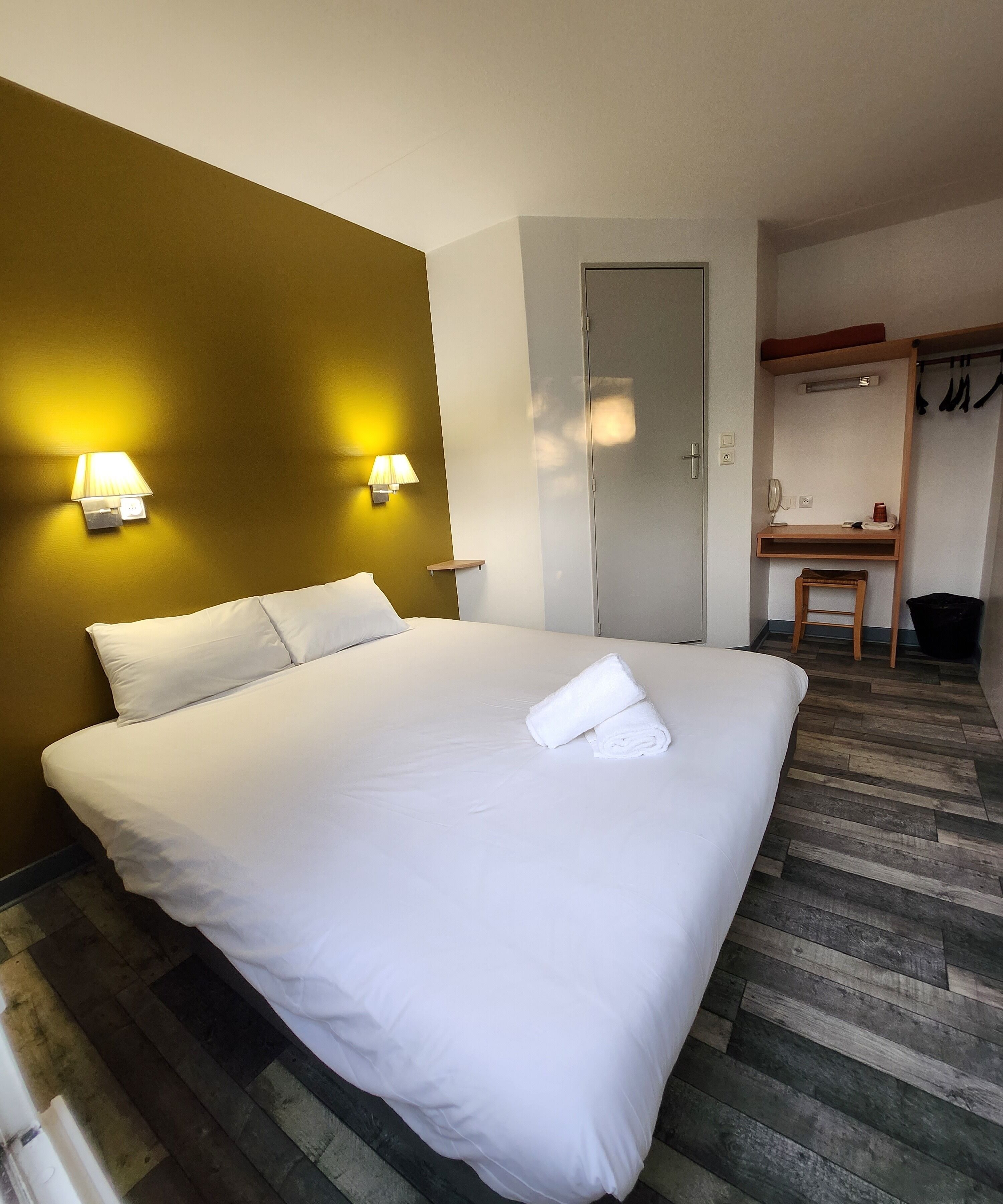A hotel room with a large bed, two bedside lamps, a wooden desk, and a wardrobe.
