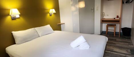 A hotel room with a large bed, two bedside lamps, a wooden desk, and a wardrobe.