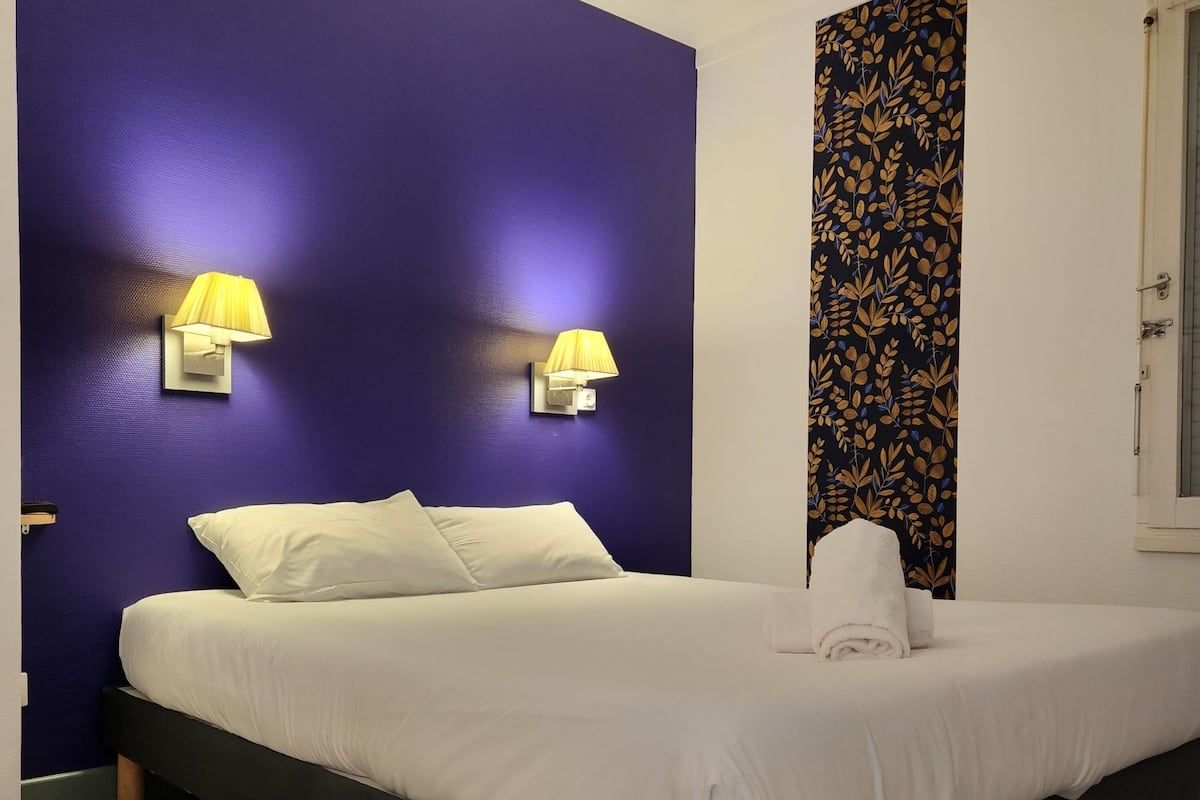 Ein Schlafzimmer mit einem großen Bett, zwei Wandlampen, einem gemusterten Vorhang und Holzdielen.