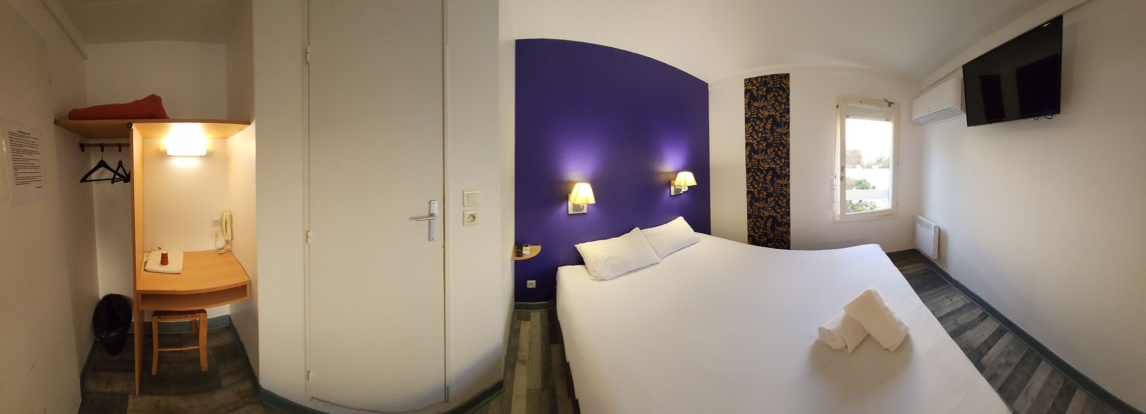 Een hotelkamer met een bed, een bureau, een stoel, een kledingkast en een badkamer.