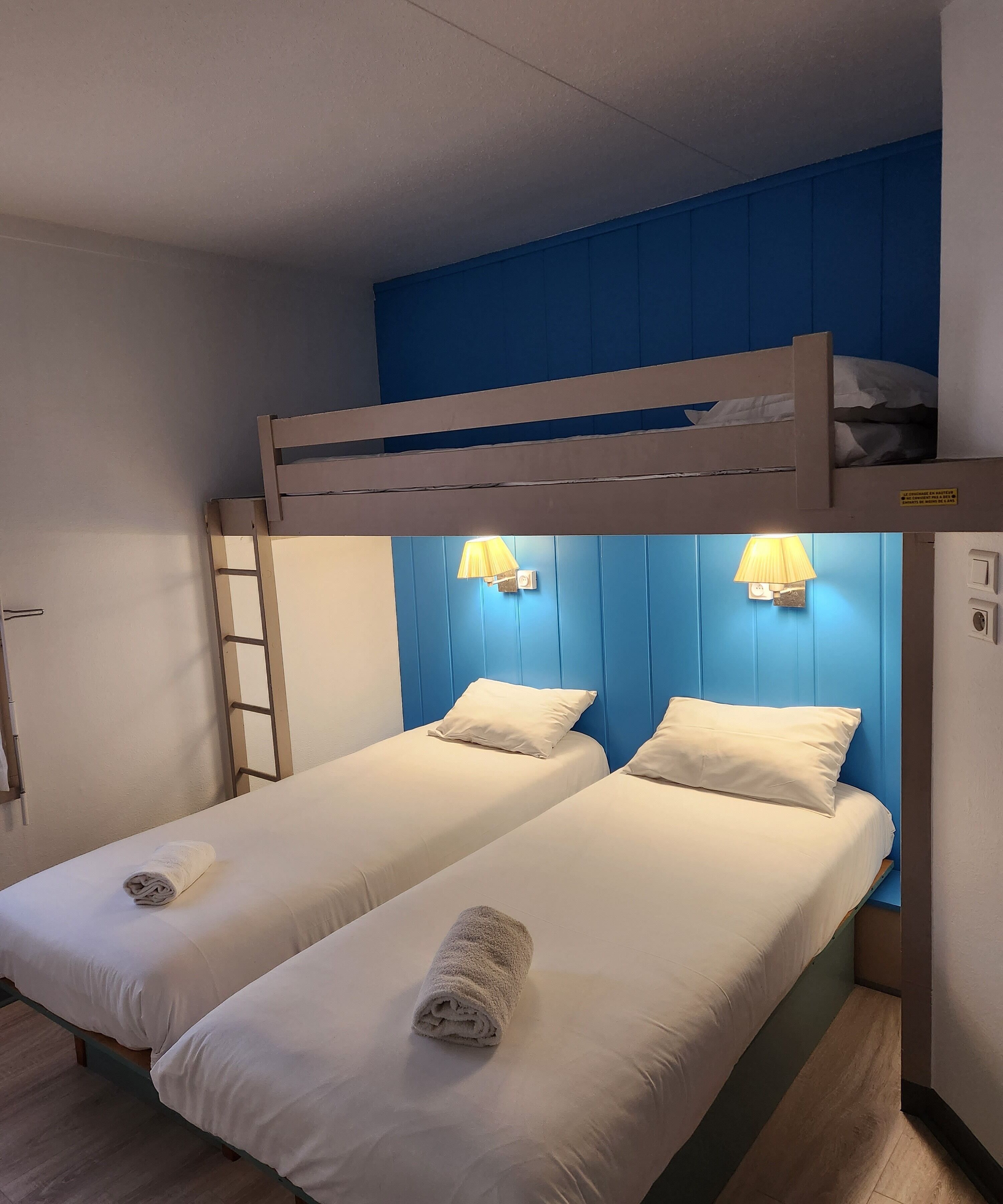 A room with two single beds, a bunk bed above, and a wooden ladder.