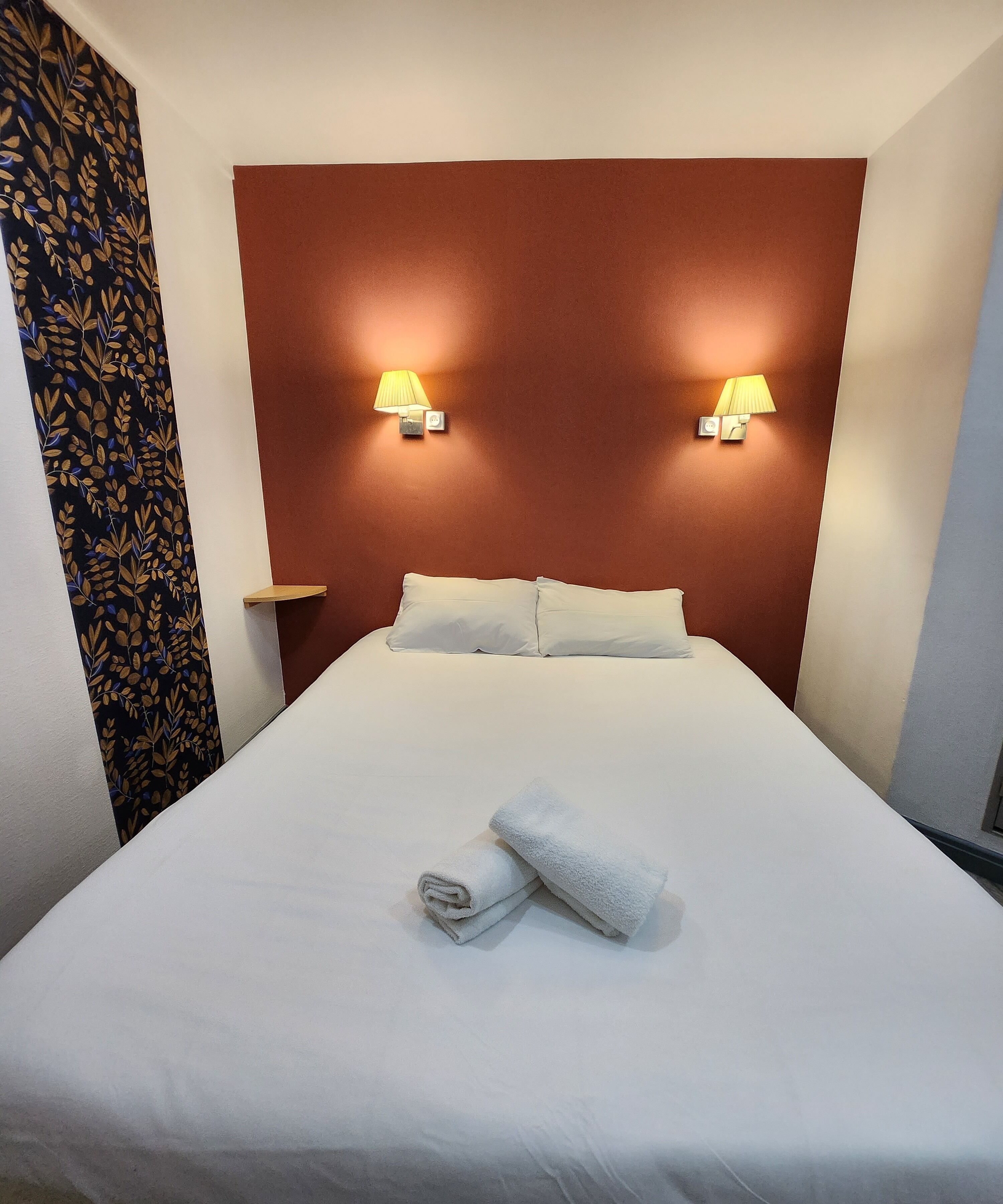 Una habitación de hotel con una cama grande, dos lámparas de noche y una cortina estampada.