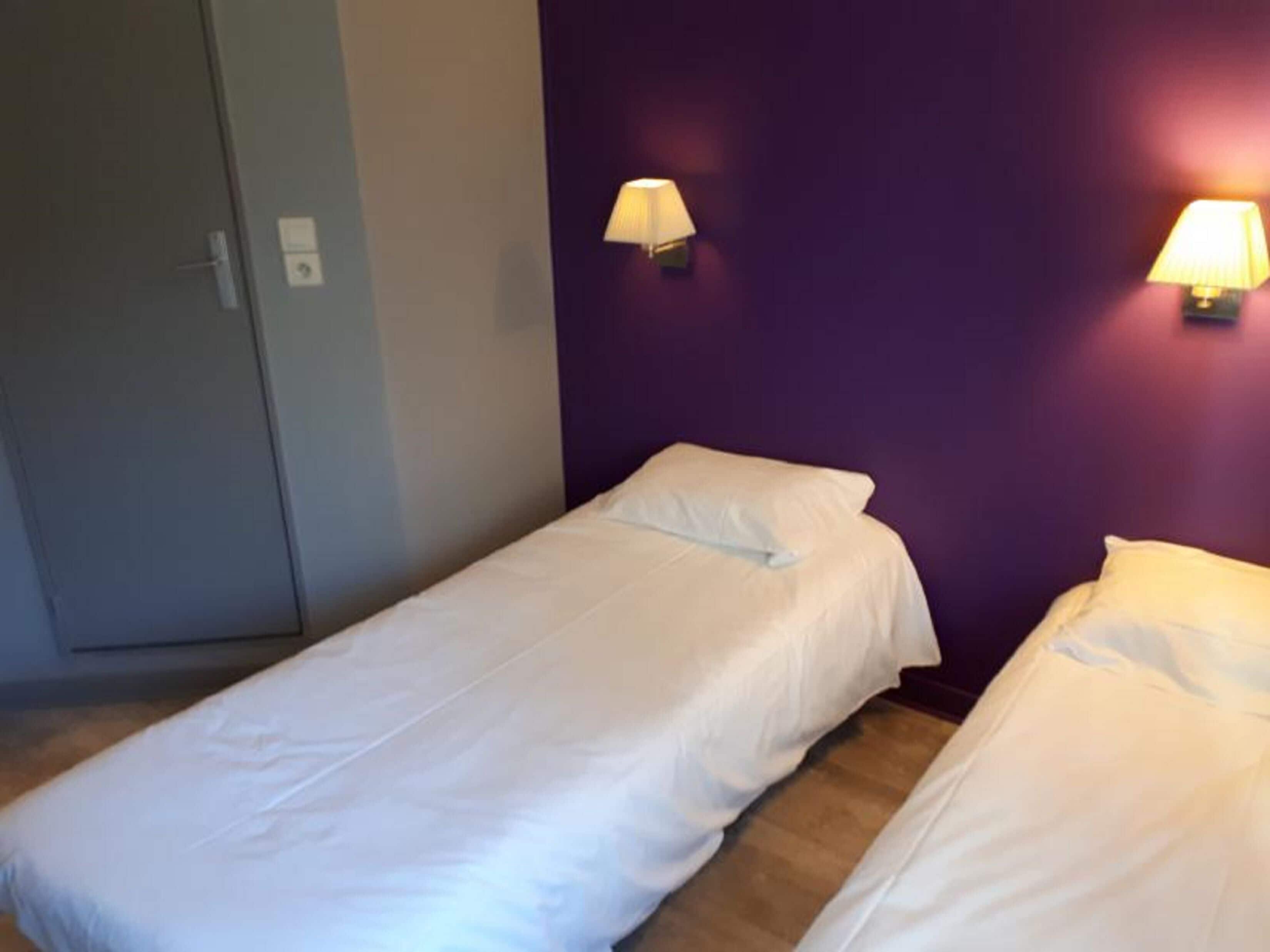A room with two single beds, a wardrobe, and two wall-mounted lamps.