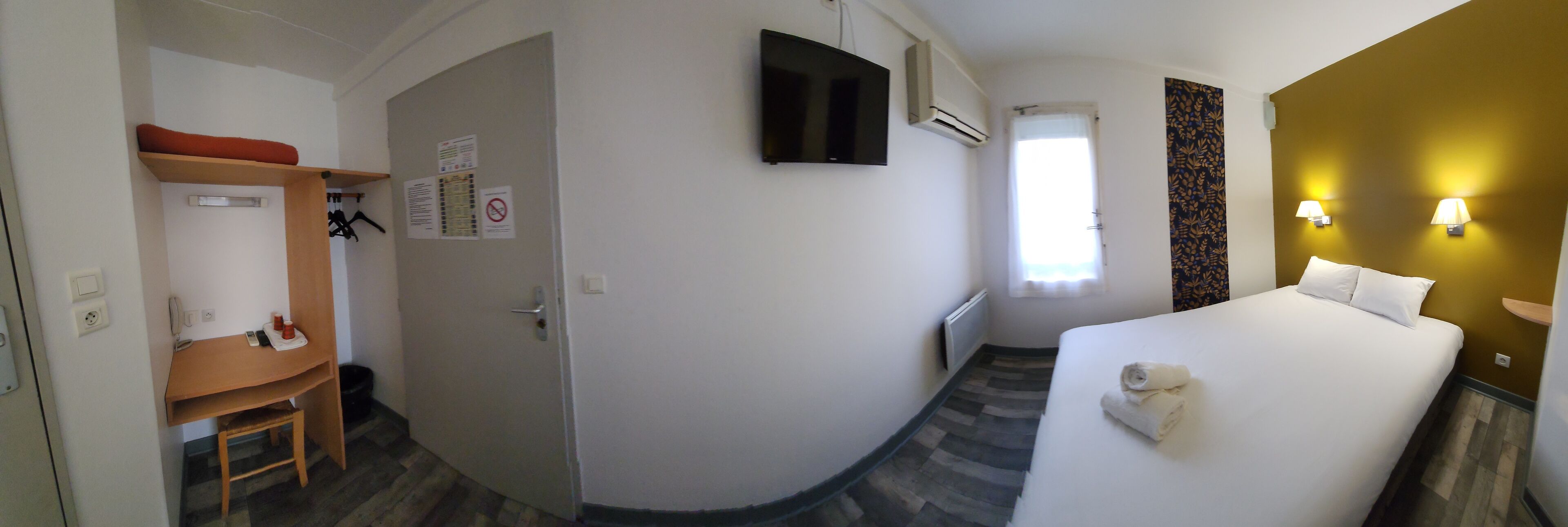 Habitación de hotel con cama, escritorio, teléfono, armario y televisor.