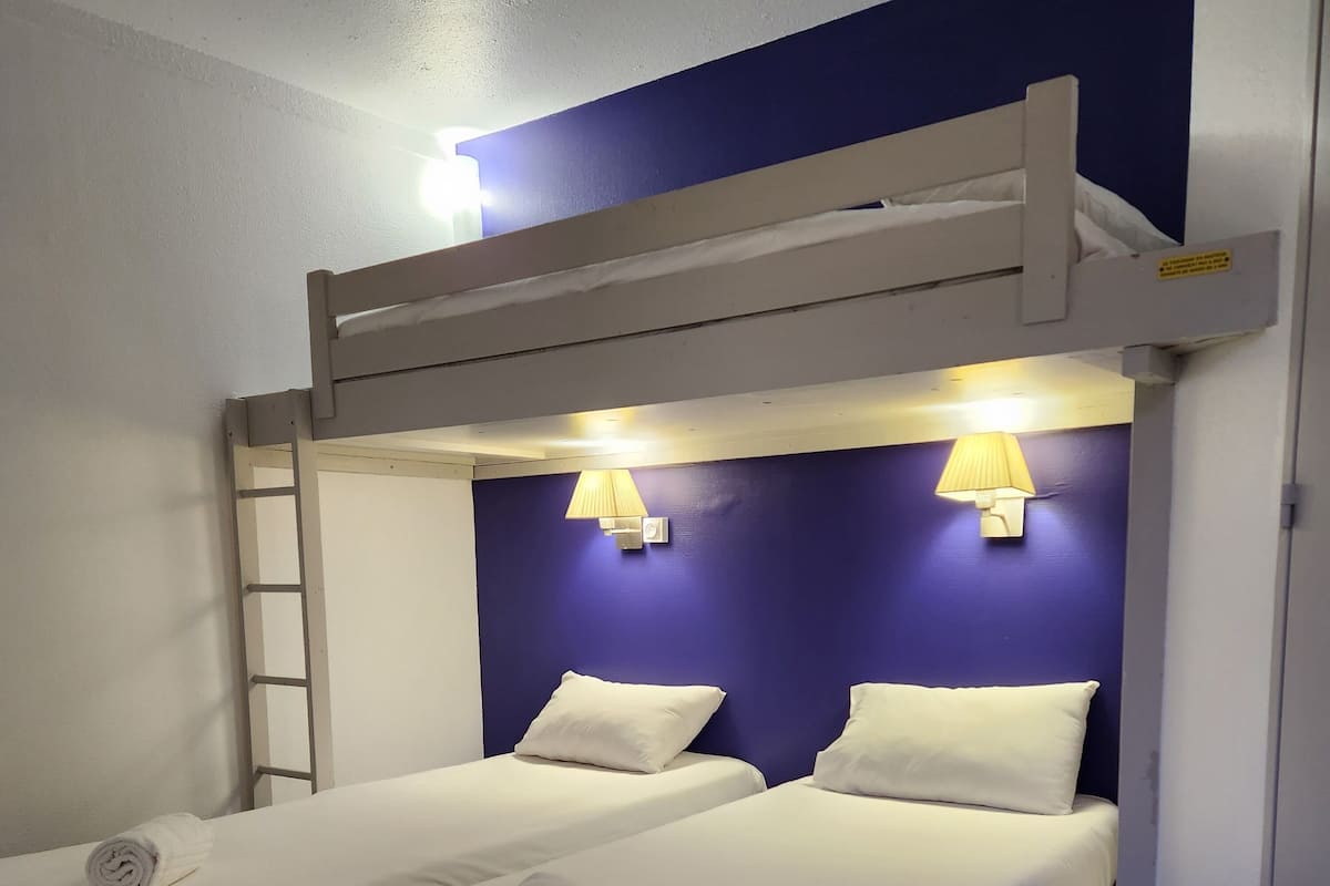 Ein Zimmer mit zwei Betten, jeweils mit weißer Bettwäsche und Kissen, einem Hochbett darüber und Holzboden.