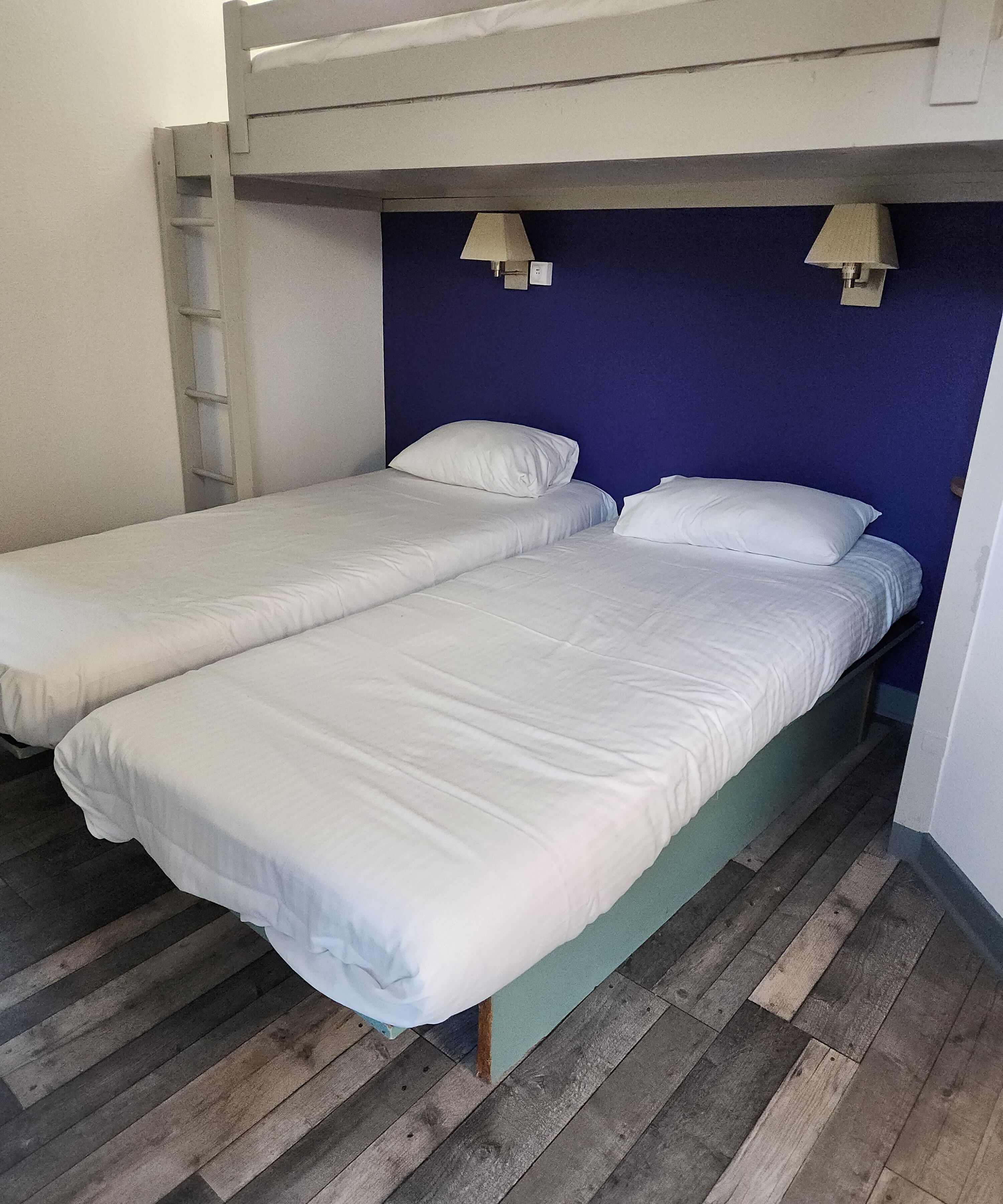 Una habitación con dos camas individuales, suelo de madera y una cama litera superior.