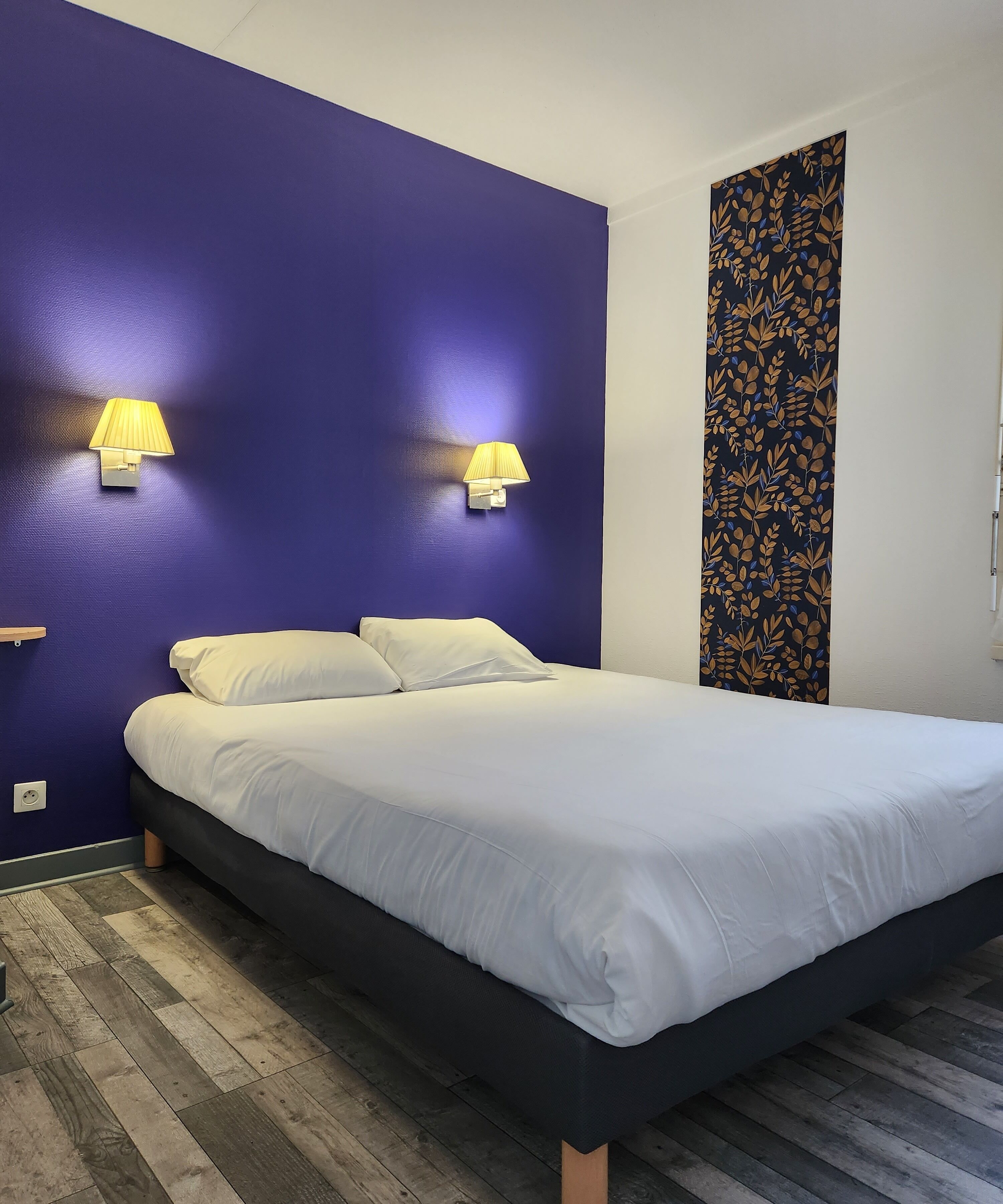 Una habitación de hotel con una cama grande, dos lámparas fijadas a la pared y un tapiz estampado.