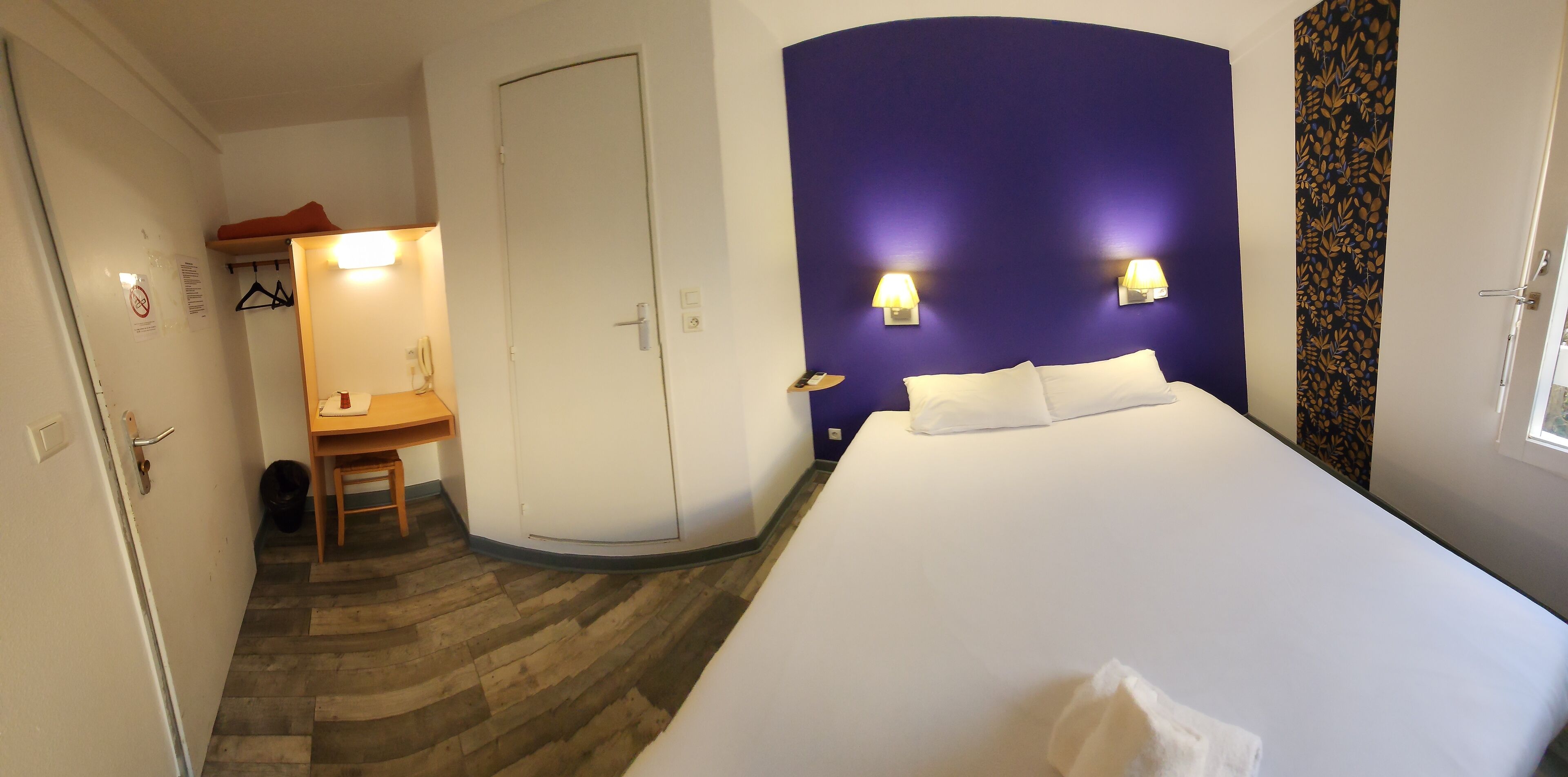 A hotel room with a bed, a desk, and a wardrobe.