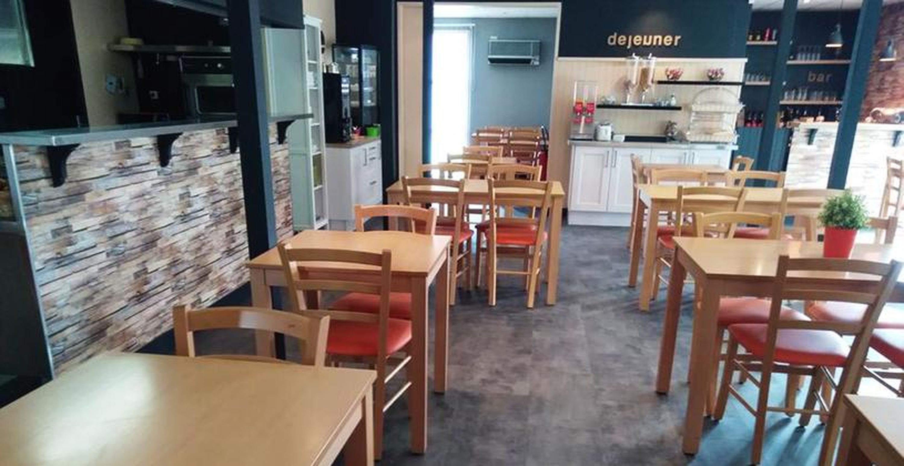 A restaurant with wooden tables and chairs, a kitchen area, and a bar.