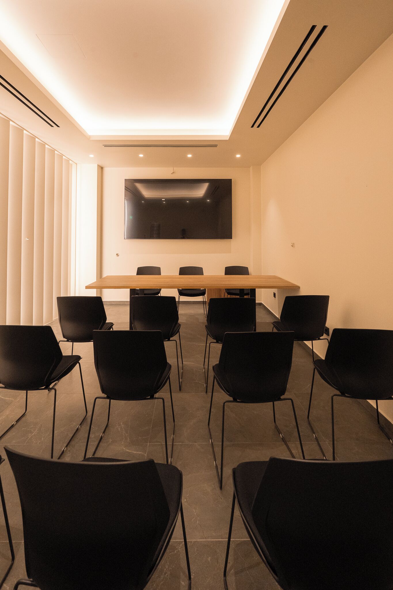 Un salón de conferencias con una larga mesa, sillas negras, un televisor de pantalla plana e iluminación empotrada en el techo.