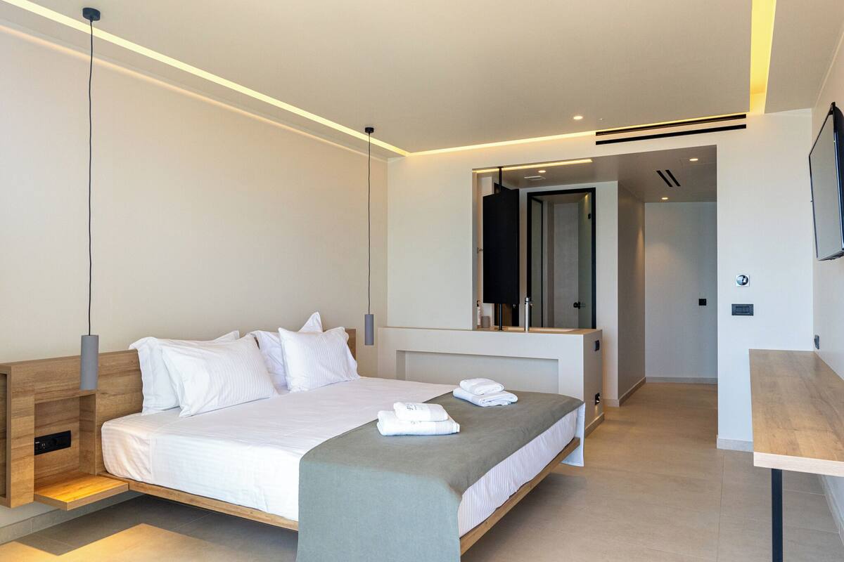 Una habitación de hotel moderna con cama, mesitas de noche, escritorio y espejo.