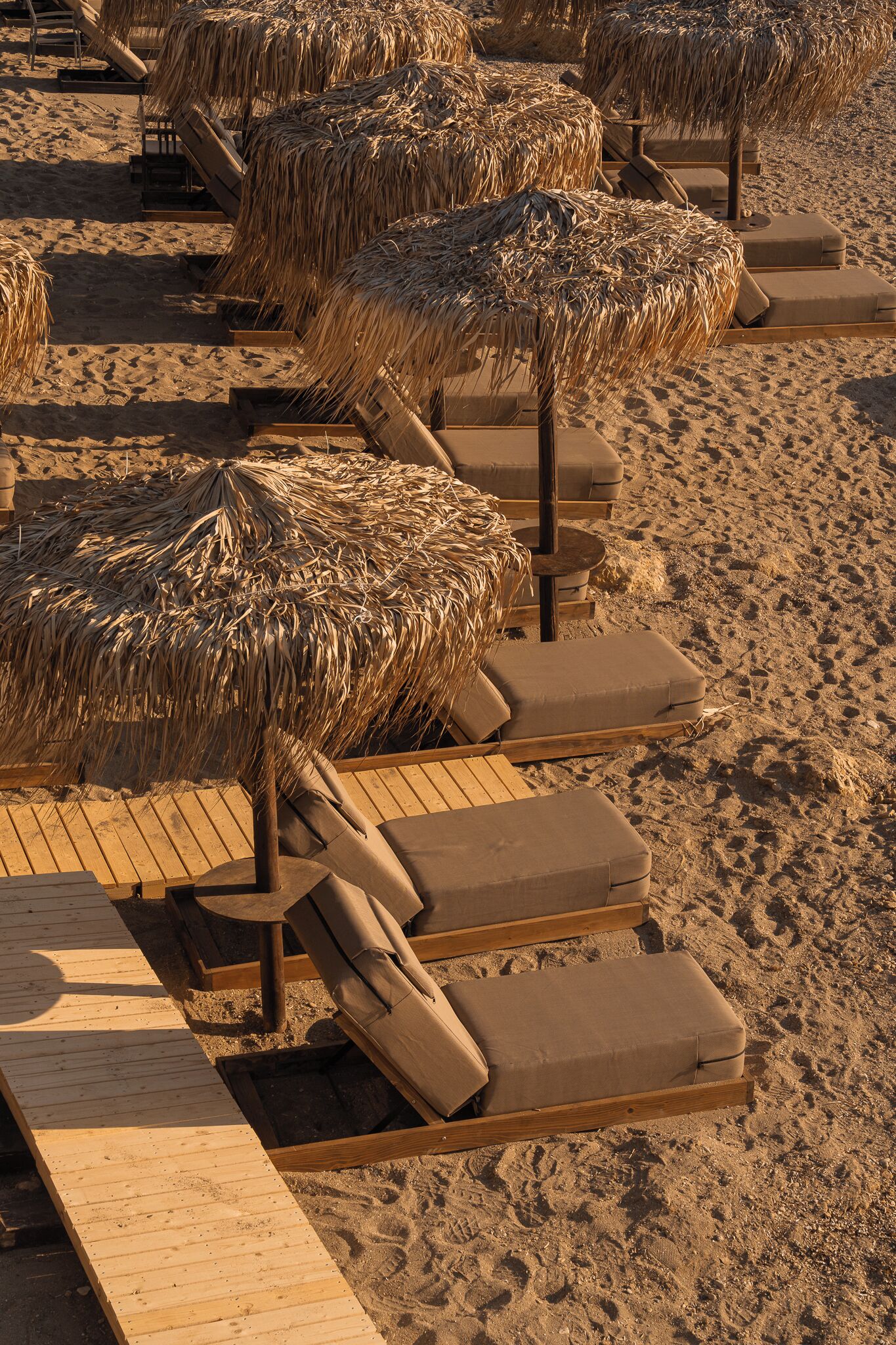 Una playa con sillones de madera y sombrillas de paja.