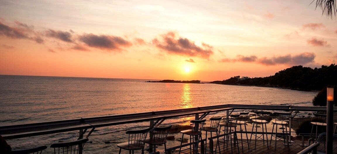 Een zonsondergang uitzicht vanaf een restaurant aan zee, met terras en een hekwerk met uitzicht op het water.