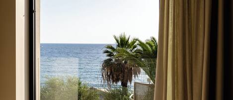 Un balcón con vista al mar, una palmera y una silla.
