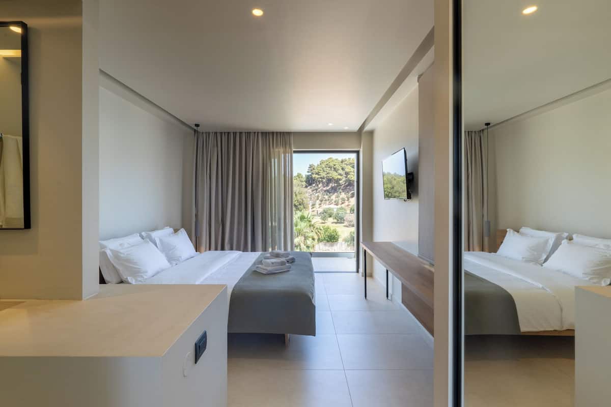 Una habitación de hotel moderna con dos camas, un ventanal con cortinas, un televisor de pantalla plana y un escritorio pequeño.