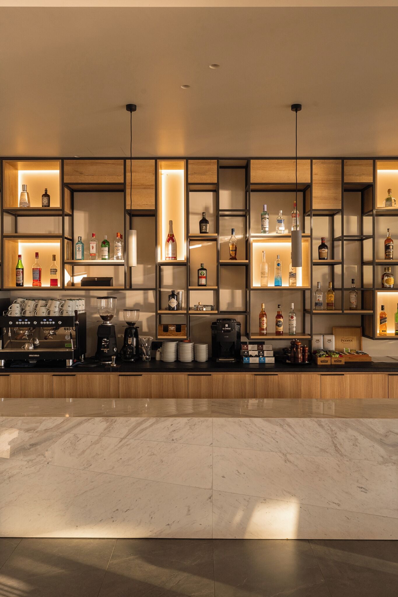 A modern bar area with shelves of liquor bottles, a coffee machine, and a marble countertop.