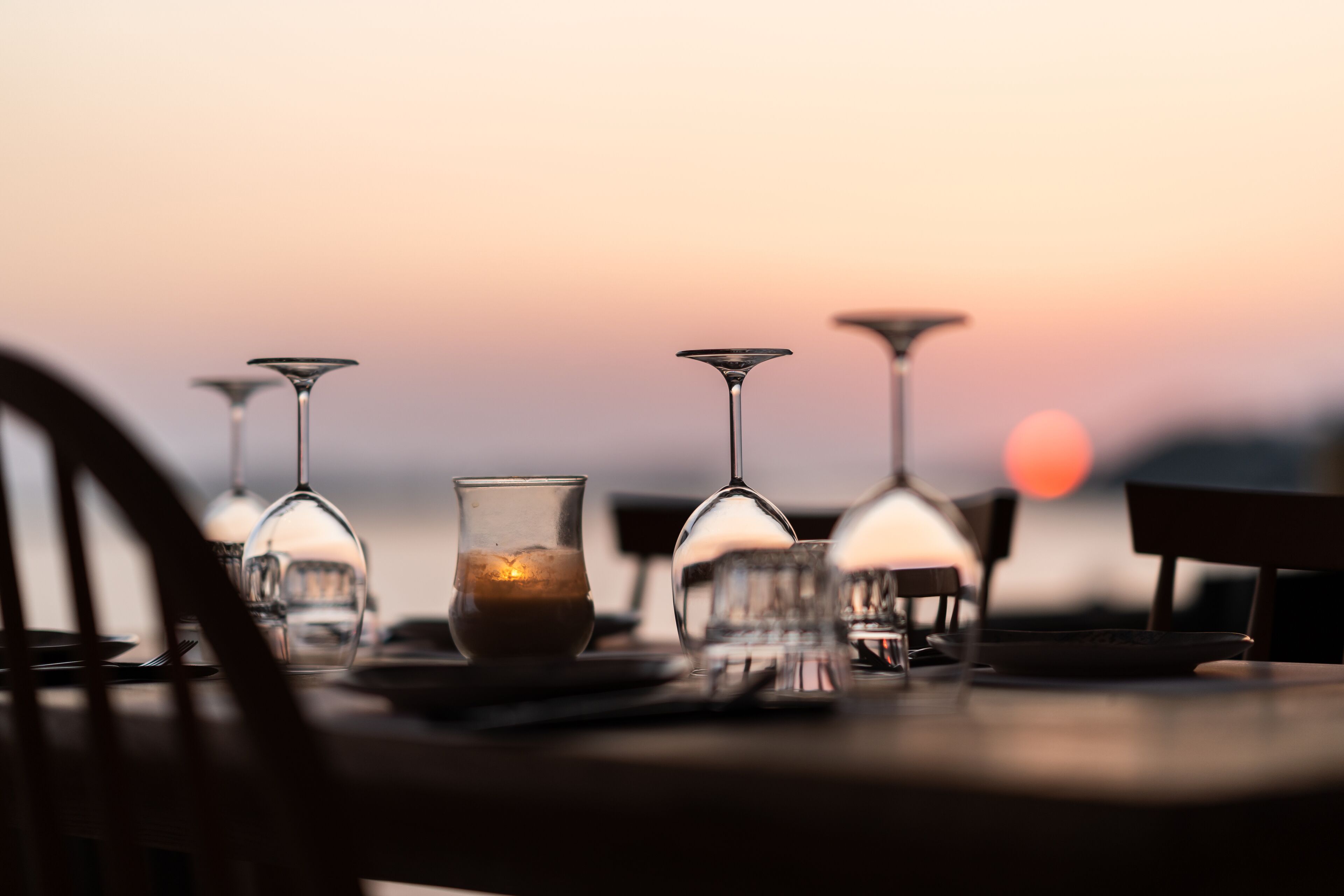 Mesa lista para cenar con copas de vino y una vela, sobre un fondo de atardecer.