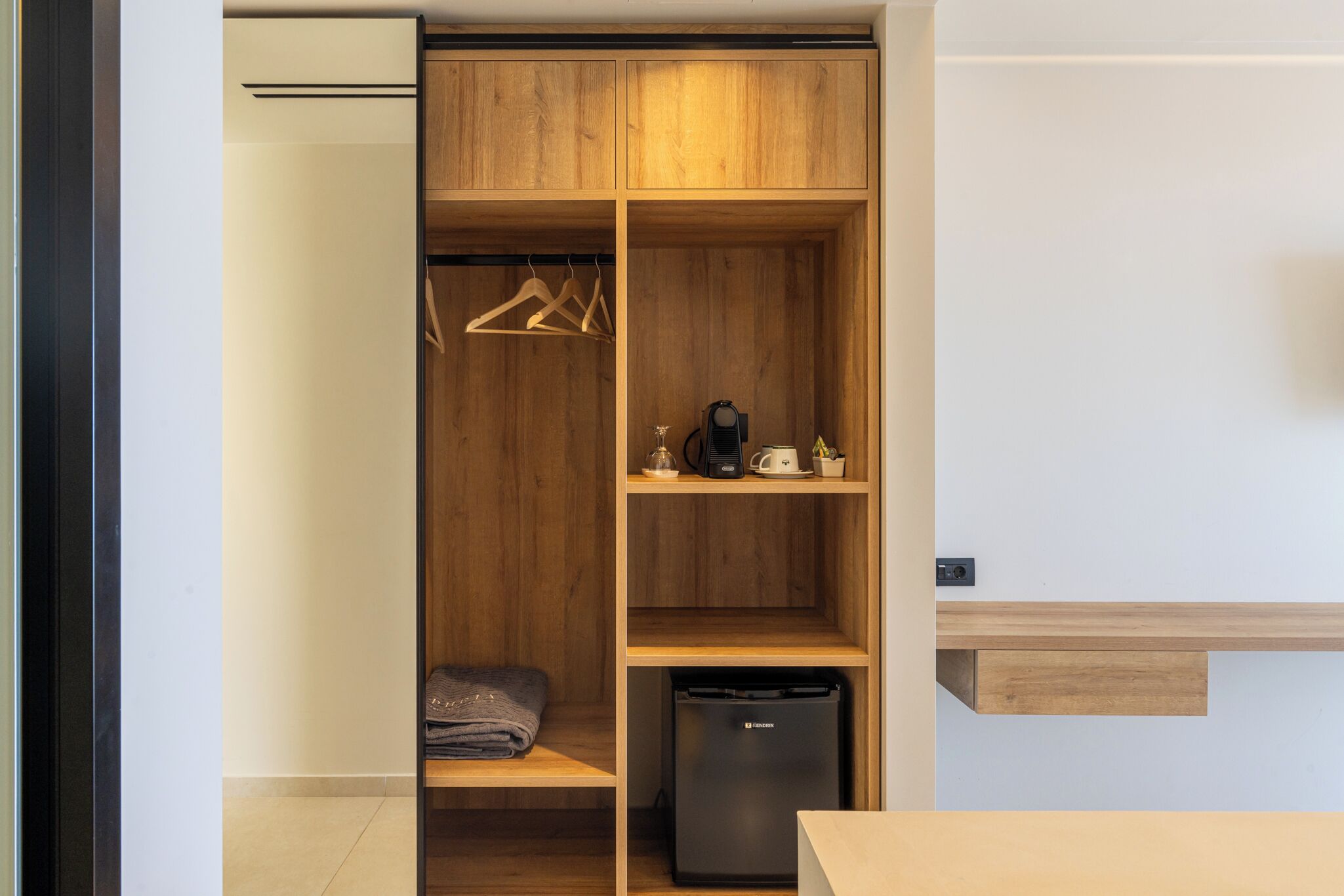 Un armario compacto y moderno con estantes de madera, barra para colgar y espacio para electrodomésticos.