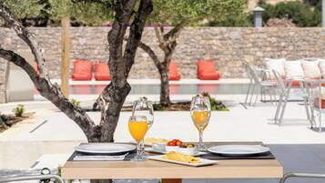 Un tavolo da pranzo all'aperto con piatti, bicchieri e cibo, sullo sfondo un muro di pietra e alberi.